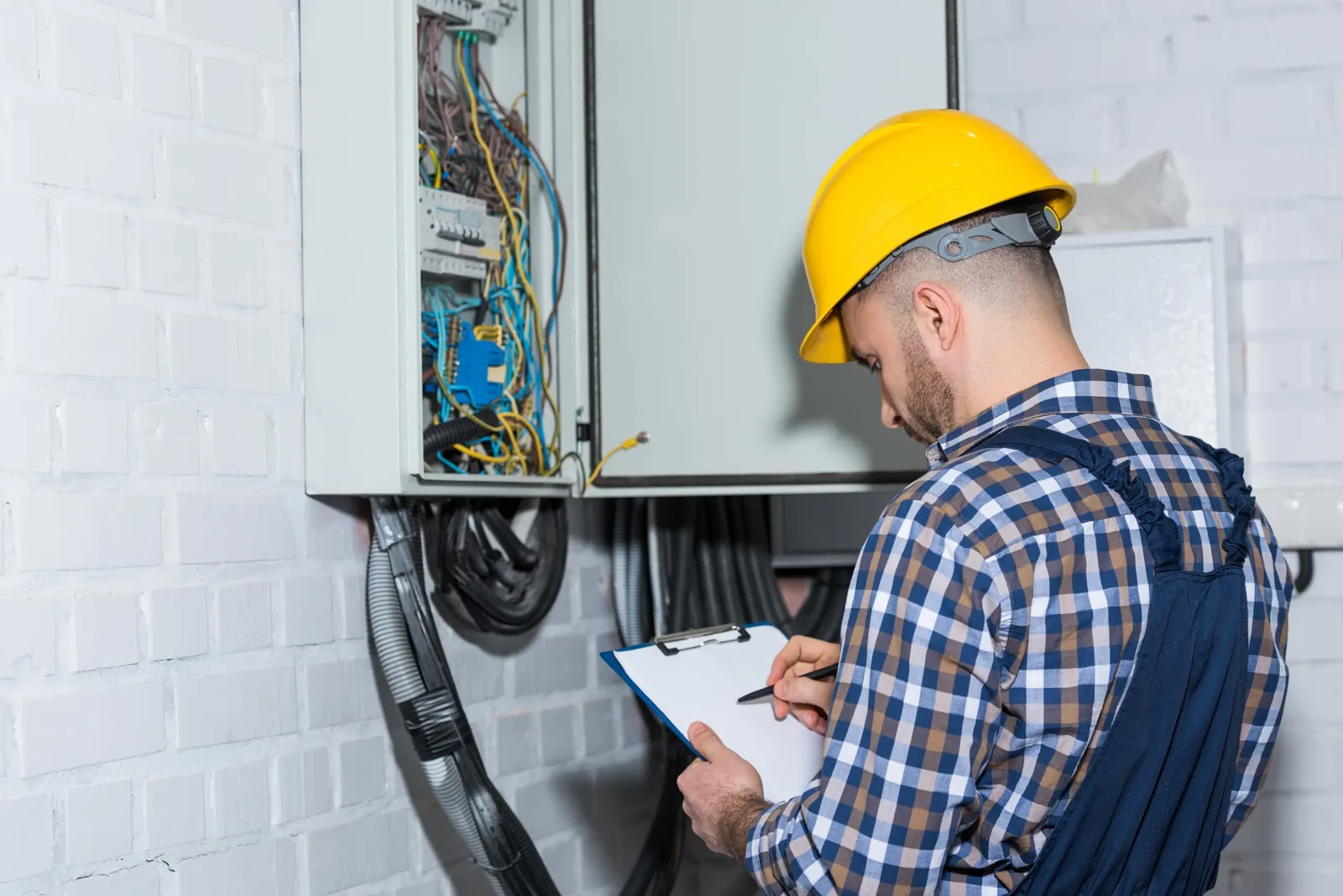 Electricista revisando un cuadro eléctrico y anotando en una carpeta